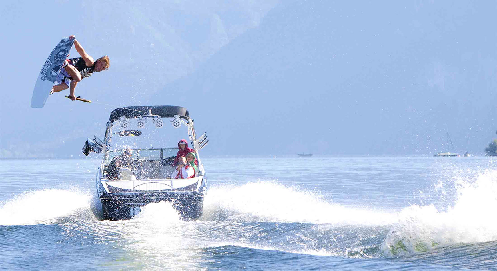 Wakeboarder springt hoch über der Welle hinter dem Boot